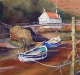 Two coble fishing boats on Staithes Beck riverbed with footbridge and cottage in background