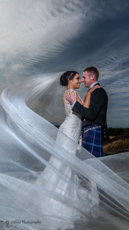 Bride and Groom in Romantic pose with a long veil. Lit by off camera flash. The reflection created in camera using a phone