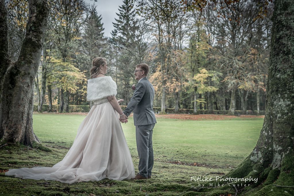 Bride & Groom holding hands in romantic pose between trees, lit using natural light.