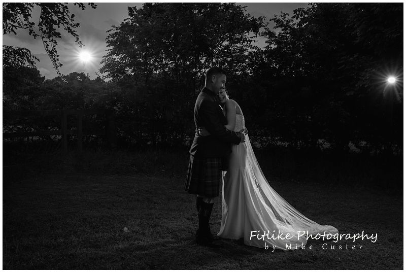 A wedding photography of the bride and groom posed with each other. Lit by 2 off camera flashes just behind and too the side of them.