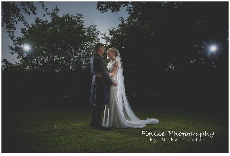 A wedding photography of the bride and groom posed with each other. Lit by 2 off camera flashes just behind and too the side of them.