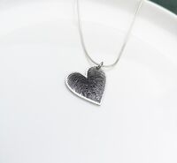 Ink fingerprints from 2 children merged on a heart pendant.