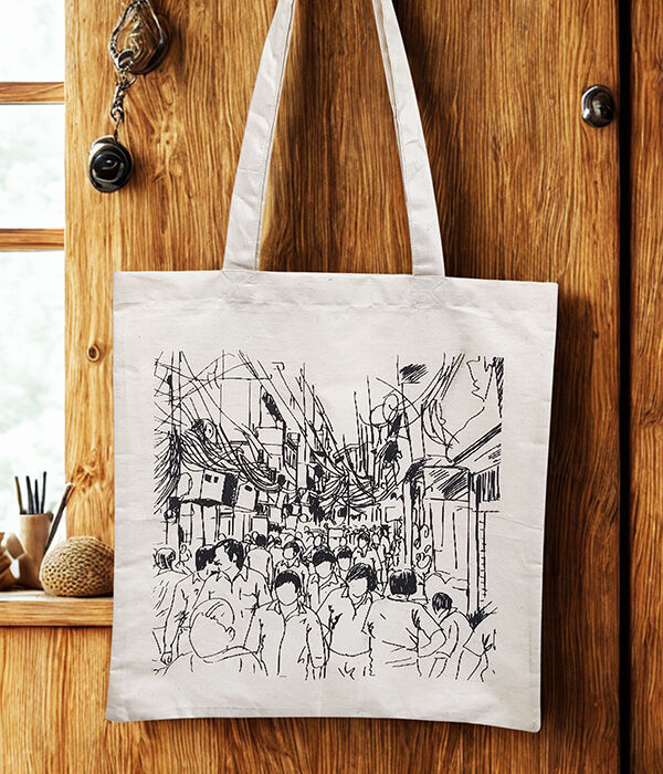 A cotton tote bag with a print of a busy old Delhi street is hanging from a door.