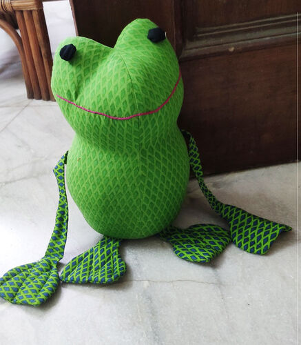 Green fabric frog doorstop with two long legs sitting in front of an open door