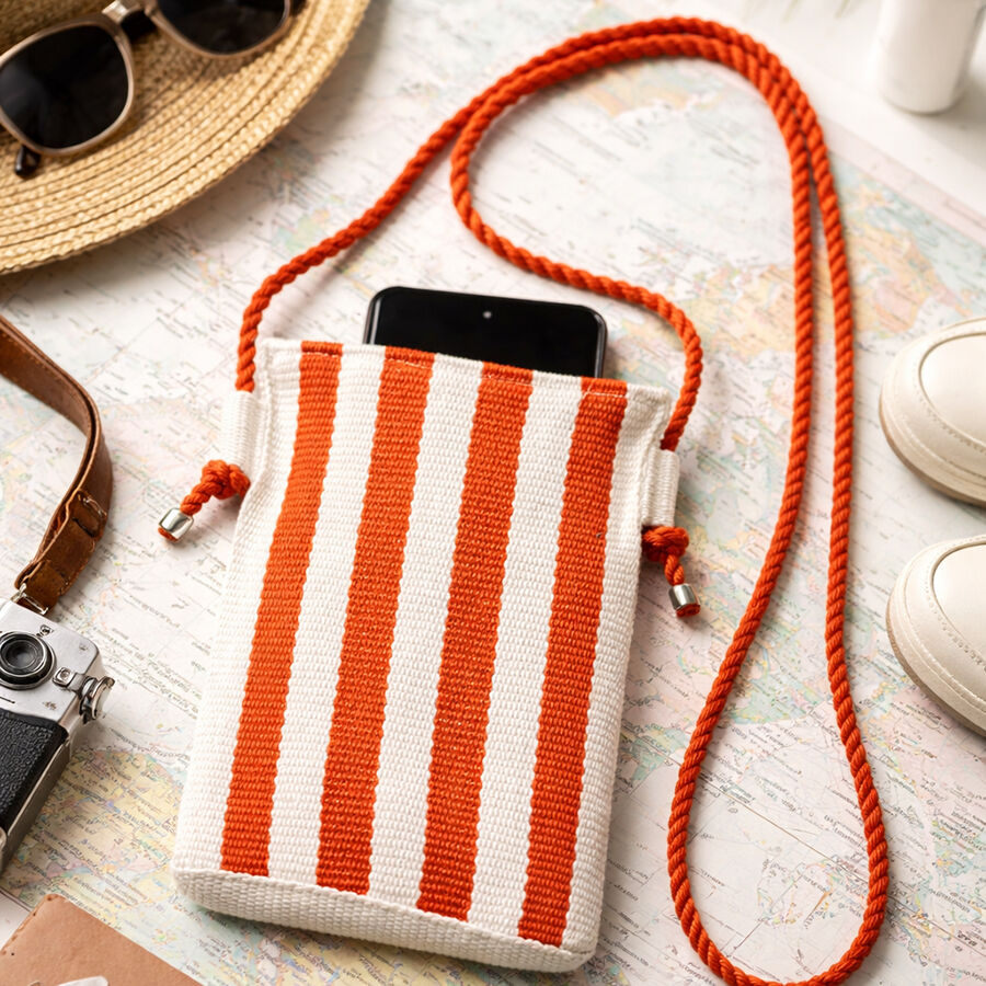 Orange and white striped mobile phone sling bag on a white surface with c acamera and sunglasses