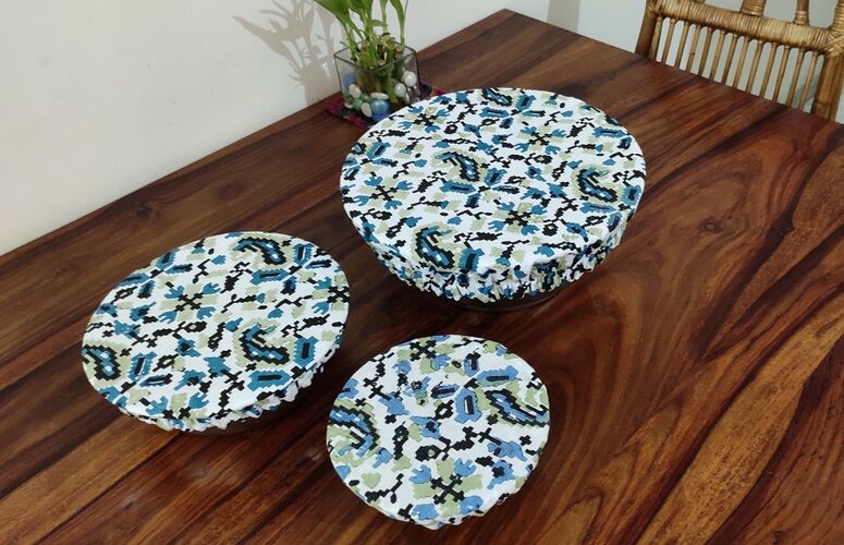 Three bowls on a wooden table all covered in organic cotton printed bowl covers. The design on the covers is white with blue and black ikat desig. One bowl is oval, the others are roundand different sizes.