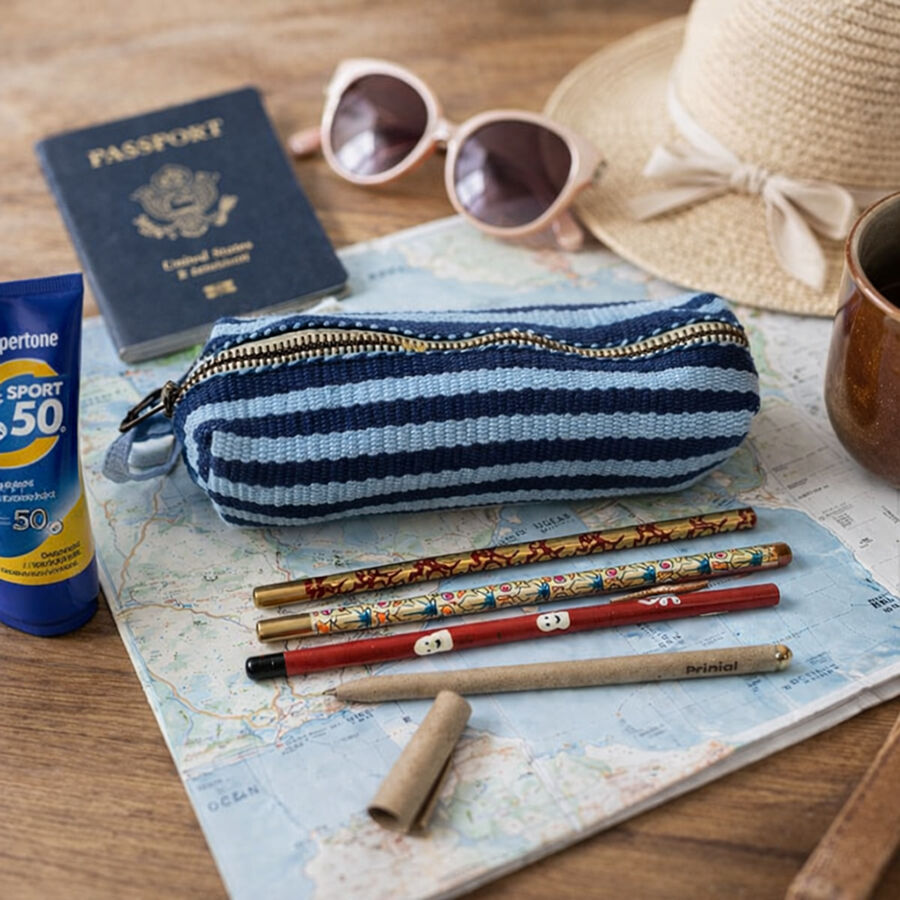 Blue striped pencil case resting on a mapwith some hand painted pencils nearby, passport, sun hat and some sun cream