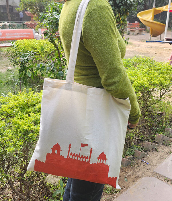 A woman carrying a cotton tote bag with a print of the red fort on the front.
