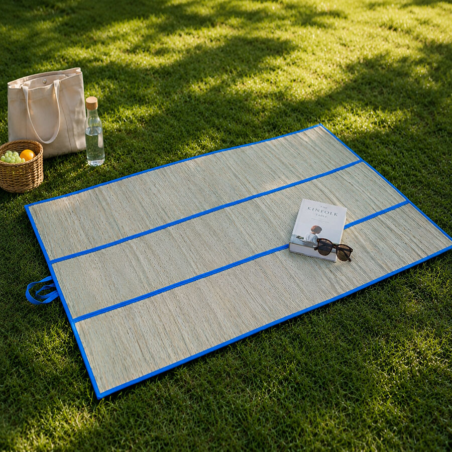 A folding mat made of water hycinth open flat on a patch of shady grass.
