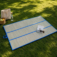 A folding mat made of water hycinth open flat on a patch of shady grass.