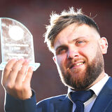 Portrait of a young bearded man in shirt and tie holding an award he has won
