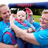 A baby gets a medal with mother and grandmother at an Alzheimer's Society Memory Walk event photography by Thousand Word Media Gloucestershire.