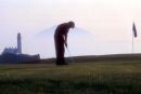 A golfer on the Turnberry golf course with the iconic lighhouse and Ailsa Craig in the photo
