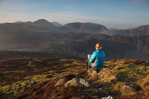 04D-5174 Woman on Fleetwith Pike Reading a Book in Early Morning Light with the View South Towards the Mountains of Great Gable and Kirk Fell Lake District Cumbria UK.
