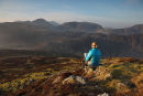 04D-5174 Woman on Fleetwith Pike Reading a Book in Early Morning Light with the View South Towards the Mountains of Great Gable and Kirk Fell Lake District Cumbria UK.