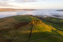 The tree covered ancient burial mound of Kirkcarrion illuminated by the setting sun, Teesdale, County Durham, UK.