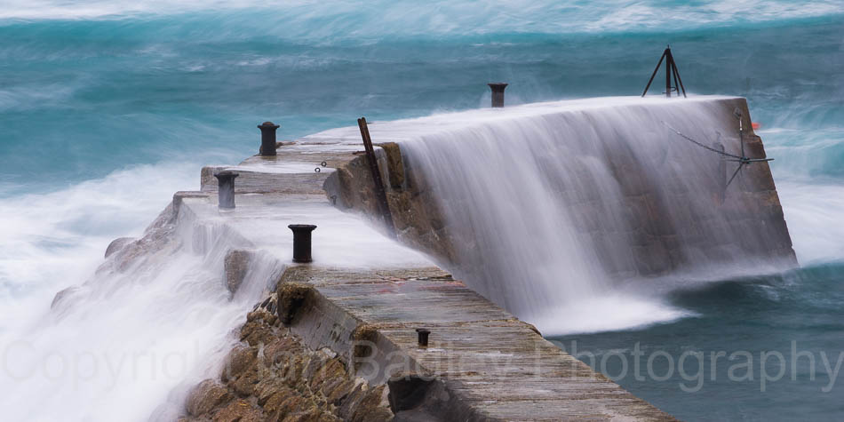 Rough seas crashing over the sea wall at Sennan Cove, Cornwall, England