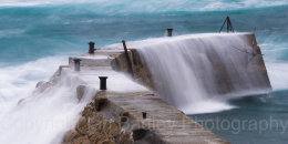 Rough seas crashing over the sea wall at Sennan Cove, Cornwall, England