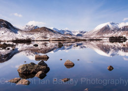 Still loch and rocks at first light over snow covered mountains, Rannoch moor, scotland