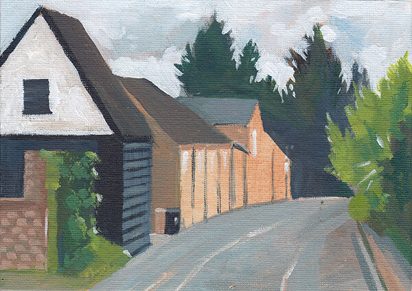 a narrow, curving road with trees on one side, and a row of buildings on the other. one is black wood cladding, the rest are red brick. there are tall, dark pine trees on the horizon.