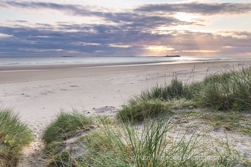 Early morning sun breaking through over Farne Islands from Bamburgh beach