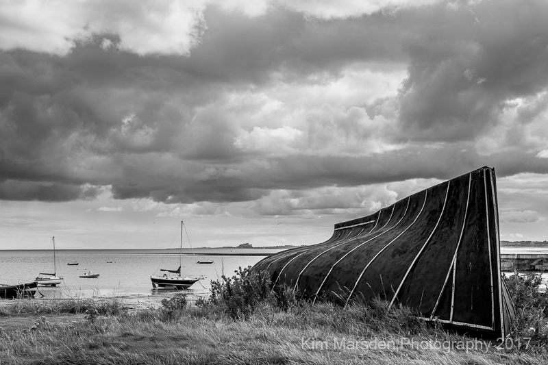 Lindisfarne boat with Bamburgh Castle in the distance - mono