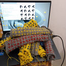 a pile of small pieces of knitting sitting on a laptop keyboard. The screen shows the knitting machine software with an array of small black motifs