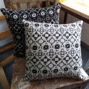 two knitted cushions, one white on black behind the other which is black on white, on an old wooden chair