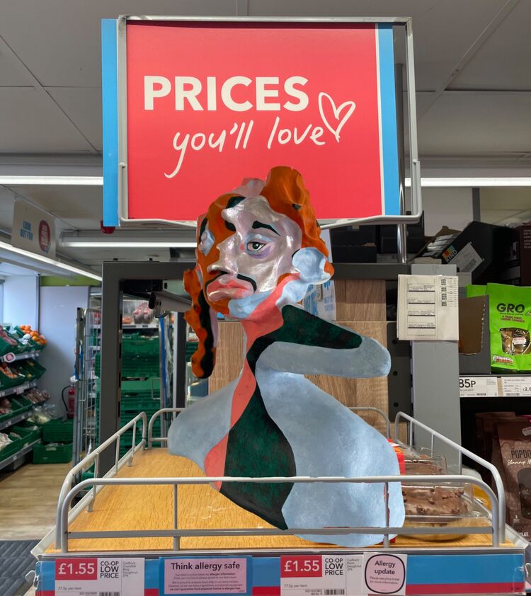 Pale blue, pink and dark green sculpture sitting on shelf in supermarket