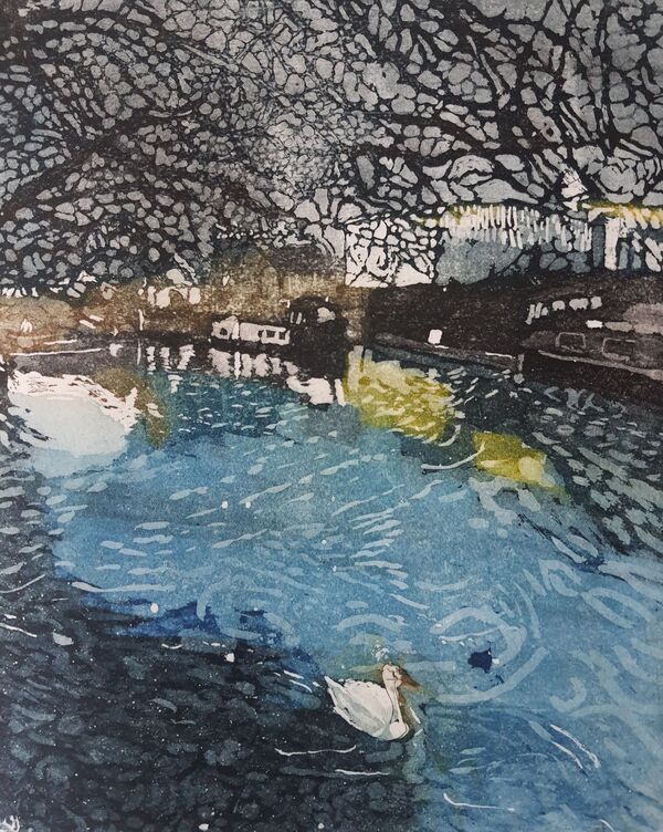 winter scene of a blue sunny river with a swan and a coot swimming. There are lacy trees and buildings in the backhround