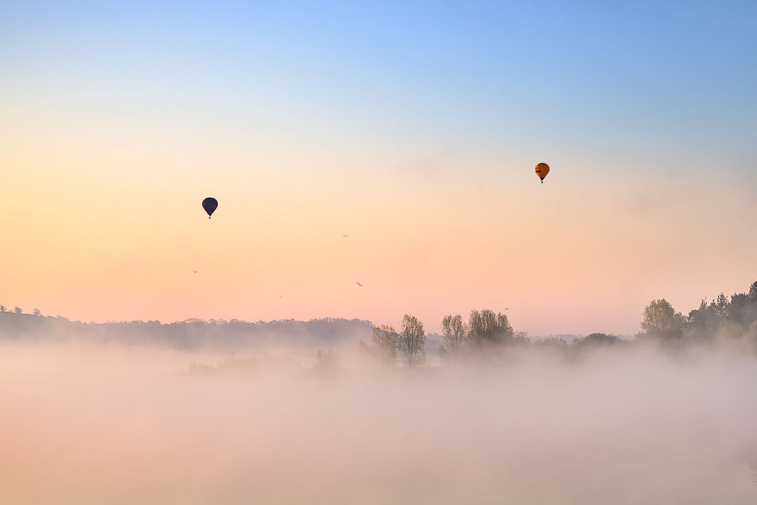 Hot air balloons drifting above low-lying mist on Chew Valley Lake at dawn in Somerset, near Bristol