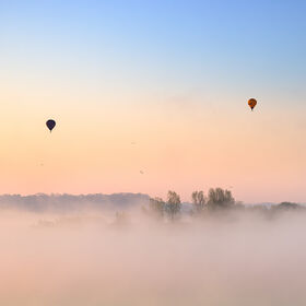 Hot air balloons drifting above low-lying mist on Chew Valley Lake at dawn in Somerset, near Bristol