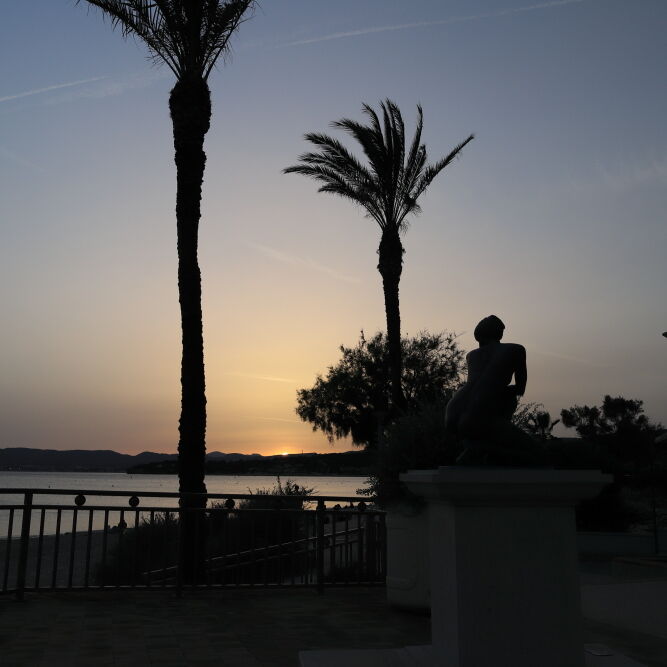 Palm tree, statue seen in silhouette at Place Città della Pieve, Les Lecques