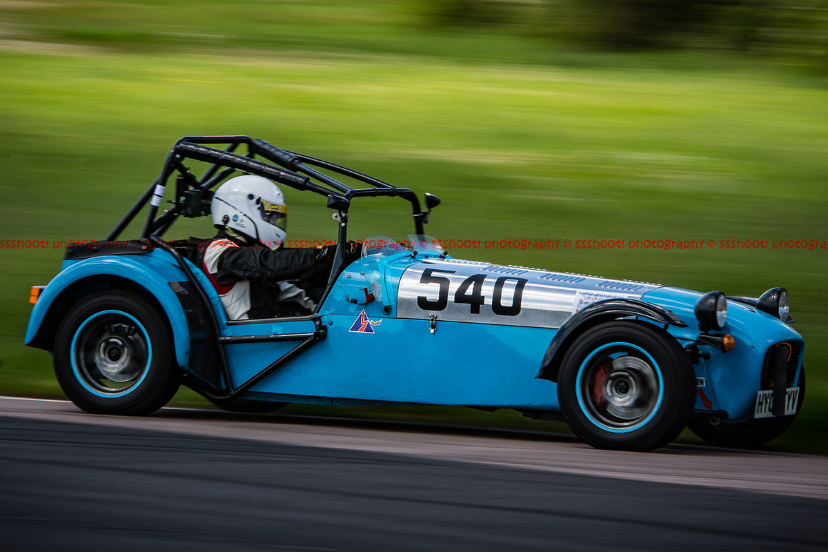 Blue caterham 7 at speed approaching flag pole corner at curborough sprint course