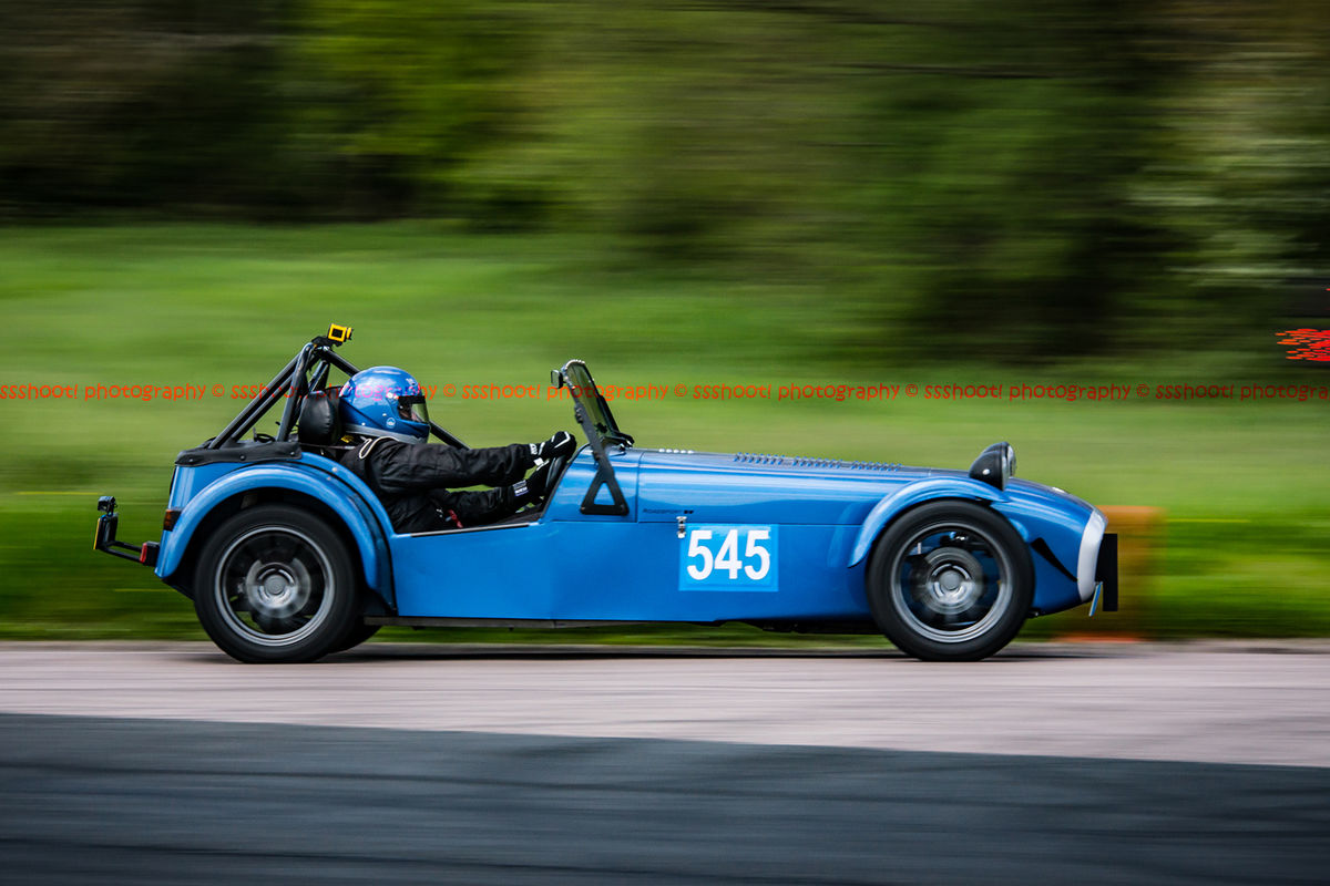 Blue caterham 7 at speed approaching flag pole corner at curborough sprint course