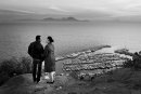 a man and a woman standing on the cliff overlooking the yacht port