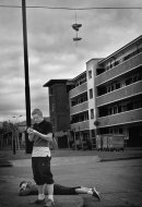 young man stands while otherone lays facedown and rests on the siedewalk with a block in the background