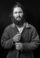 Portrait of young bearded man with a walking stick, a pilgrim, rests his hands on a walking stick