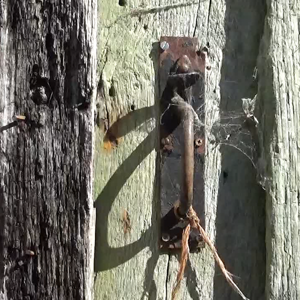 a rusty door latch on an old barn door with strong shadows